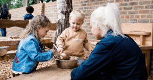 nursery practitioner and children playing in garden