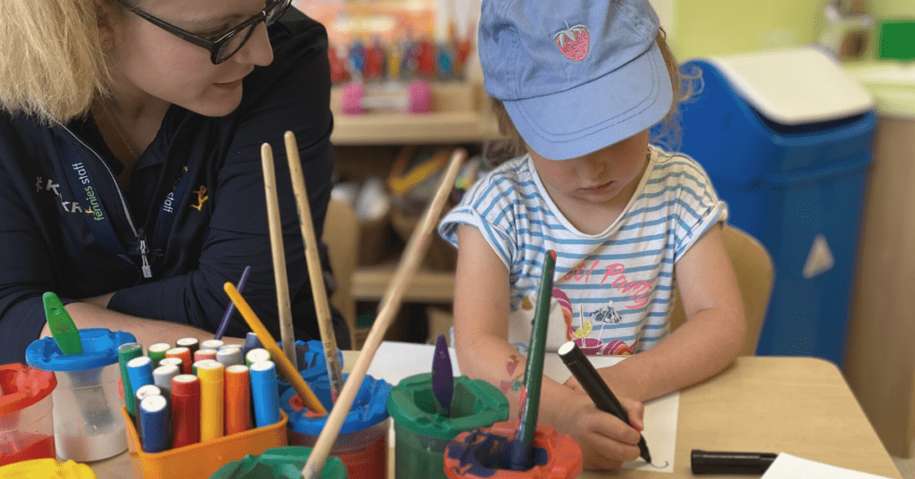 child painting in nursery with early years practitioner