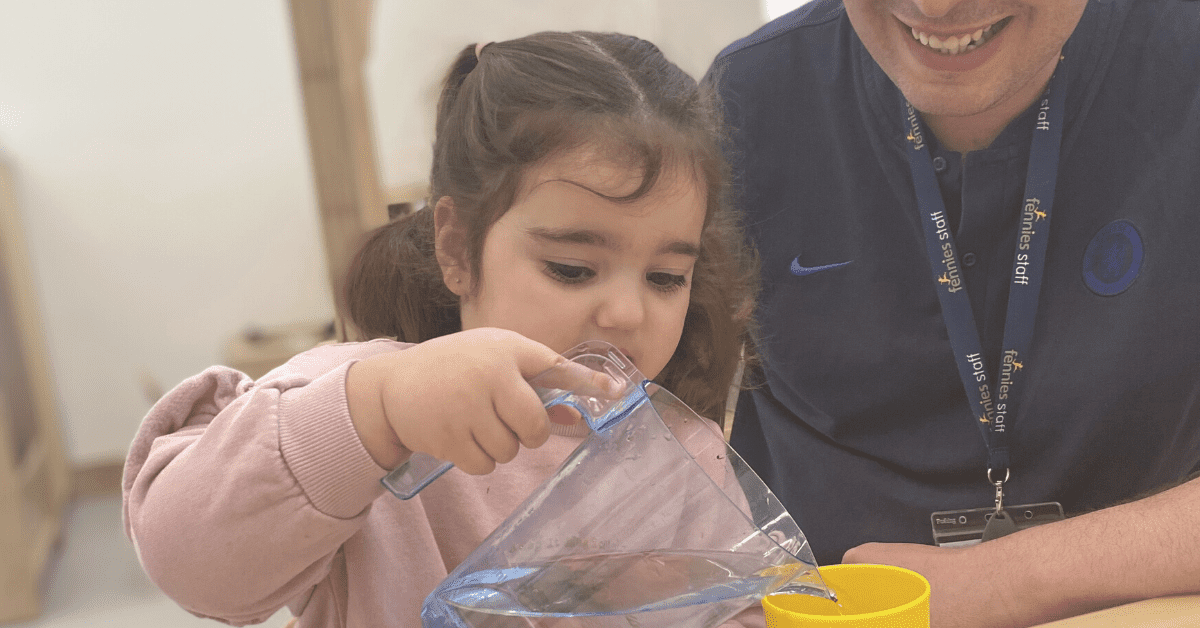 child pouring a glass of water with early years teacher