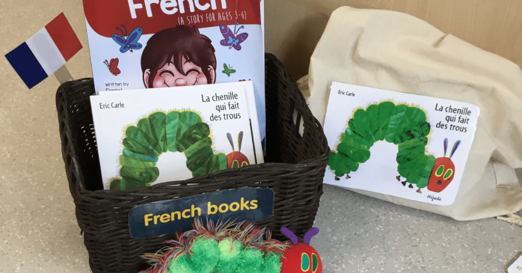 A display of french children's books in a basket labeled "french books," including titles by eric carle. a plush caterpillar toy and french flags accompany the books.