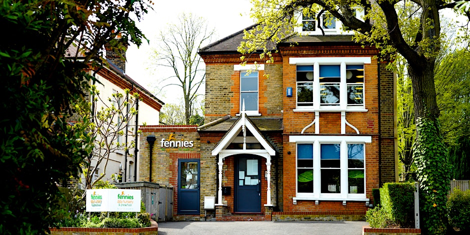 A view of a two-story brick house with a black front door, large windows, and surrounded by lush greenery, featuring signs that read "fennies.