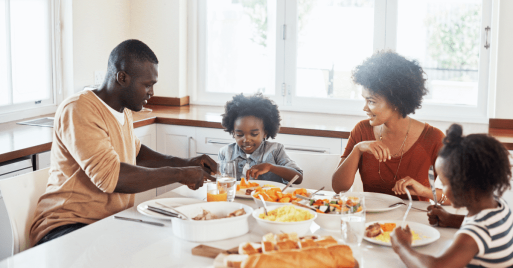 A joyful family of four sharing a healthy meal at a dining table, with smiling parents and two young children enjoying their time together in a bright kitchen.